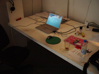 bild meiens schreibtischs um 2004. man sieht ein macbook mit maus, ein ericson handy, eine flashe parf&uuml;m und viele kabel