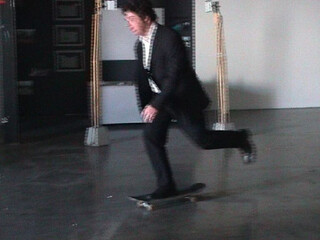 videostill aus einem kurzen video in dem ich mit einem anzug und lederschuhen kurz auf einem skateboard rumtolle