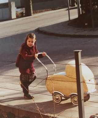elena auf dem gehweg des gangolfwegs in kornilim&uuml;ster. foto ungef&auml;hr um das  jahr 1980. sie schibet einen kinderwagen und scheint sich zu freuen.