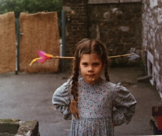 elena zuhause auf unserer terrasse in kornilim&uuml;ster. foto ungef&auml;hr um das  jahr 1980. sie tr&auml;gt ein einen schwerzartikel pfeil auf dem kopf und es sieht aus, als habe dieser pfeil ihren kopf durchbohrt.