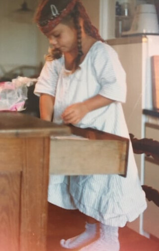 elena bei uns zuhause in kornilim&uuml;ster. foto ungef&auml;hr um das  jahr 1980. sie sortiert besteck aus der sp&uuml;lmaschine in unsere besteckschublade ein. sie tr&auml;gt ein r&ouml;tliches strinband und sieht sehr konzentriert aus.