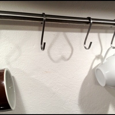 das bild zeigt einen schatten an einer weissen wand von zwei ikea-küchen-hacken. der schatten formt ein herz, das auf dem kpf steht.
