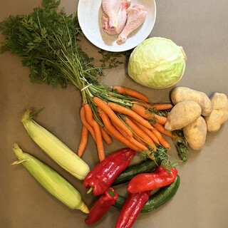 einkauf auf dem wochenmarkt, man sieht ein bund möhren, zwei maiskolben, vier spitzpaprika, vier dicke kartoffeln und einen weisskohl. ausserdem drei hähnchenbeine.