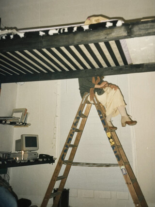 mein studentenzimmer in stuttgart um 1995. man sieht ein sehr hohes hochbett, hinter dem eine leiter steht auf der eine frau sitzt