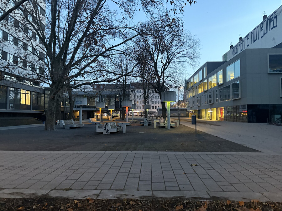 foto vom leopoldplatz. man sieht die leuchtende schillerbibliothek, farbig schimmernde betaon-strassenleuchten und auch am rathhaus ist licht