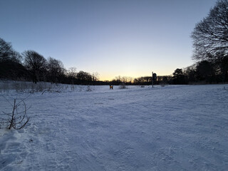 foto von der grossen wiese in den rehbergen, die wiese ist mit festgetretenem schnee bedeckt, im hintergrund geht langsam die sonne auf