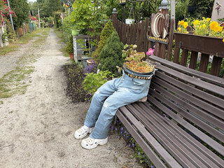 blick auf eine bank in einer gartensiedlung auf der eine mit stroh und bumen gef&uuml;llte jeans sitzt