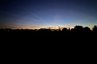 sonnenaufgang in karken mit kahlen b&auml;umen und h&auml;user-silhouetten am horizont. der himmel leuchtet blau-orange.