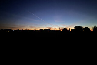 sonnenaufgang in karken mit kahlen b&auml;umen und h&auml;user-silhouetten am horizont. der himmel leuchtet blau-orange.