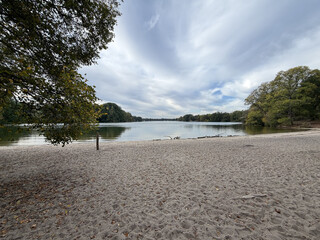 foto vom arbeiterstrand am tegeler see. das wasser ist still, der strand gelblichgrau, der himmel dramatisch bew&ouml;lkt.