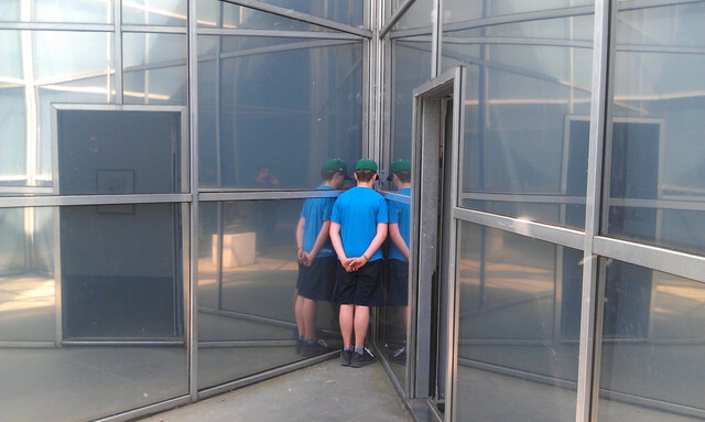 das kind steht in der spitzen ecke einer glaswand und reflektiert sich dreifach