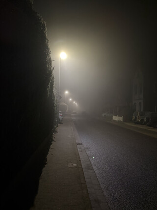 nachtbild des sehr leeren und stillen tichelkamp in karken, es ist neblig und es liegt raureif, die strassenlaternen beleuchten den nebel.
