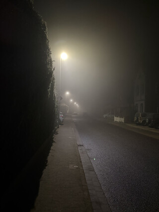 nachtbild des sehr leeren und stillen tichelkamp in karken, es ist neblig und es liegt raureif, die strassenlaternen beleuchten den nebel.