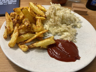 braune knsuprige pommes auf einem wiesen teller. danaben etwas krautsalat und ketchup.