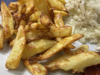 braune knsuprige pommes auf einem wiesen teller. danaben etwas krautsalat.