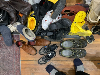 bild vom schulager neben unserer wohnungstüre. man sieht ca. 20 paar schuhe, die teilweise übereinandergestapelt liegen, ausserdem ein paar sehr grosse wandersandalen und ein paar sehr kleine halbschuhe.