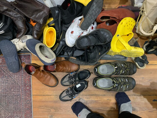 bild vom schulager neben unserer wohnungstüre. man sieht ca. 20 paar schuhe, die teilweise übereinandergestapelt liegen, ausserdem ein paar sehr grosse wandersandalen und ein paar sehr kleine halbschuhe.