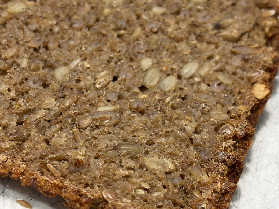 nahaufnahme einer scheibe des frisch gebackenen schwarzbrot. das brot ist sehr kornreich, aber auch fluffig-weich