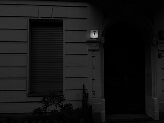 schwarzweissbild einer hausfassade mit der beleuchteten hausnummer 7.