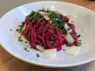 ein weisser teller mit von rote bete pesto rot gefärbten spaghetti mit etwas gehobeltem parmesan, patersilie und zitronenzesten