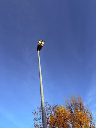 das foto zeigt einen laternenmast an dessen oberen ende ein paar LED-panels hell leuchten, obwohl der himmel taghell ist.