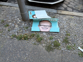 ein cdu wahlkampfplakat liegt leicht gefaltet auf dem boden. das foto des kandidaten wird dadurch verzerrt und witzig