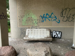 bild eines sofas vor eine graffiti besprühten betonwand. das sofa ist mit weisser wandfarbe vollgekippt.